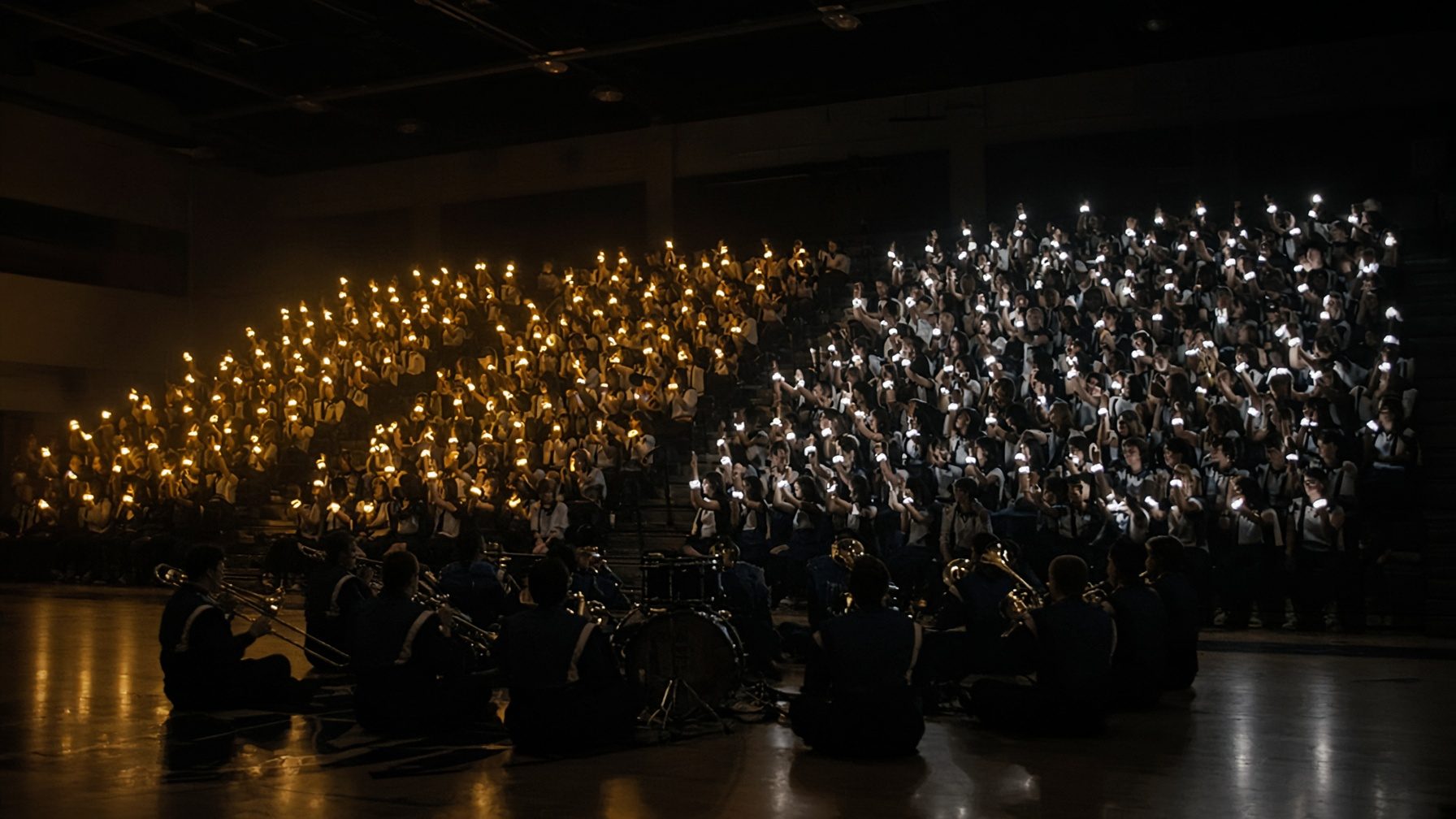 A dark gym at a pep rally, bleachers lit by gold and white LED wristbands